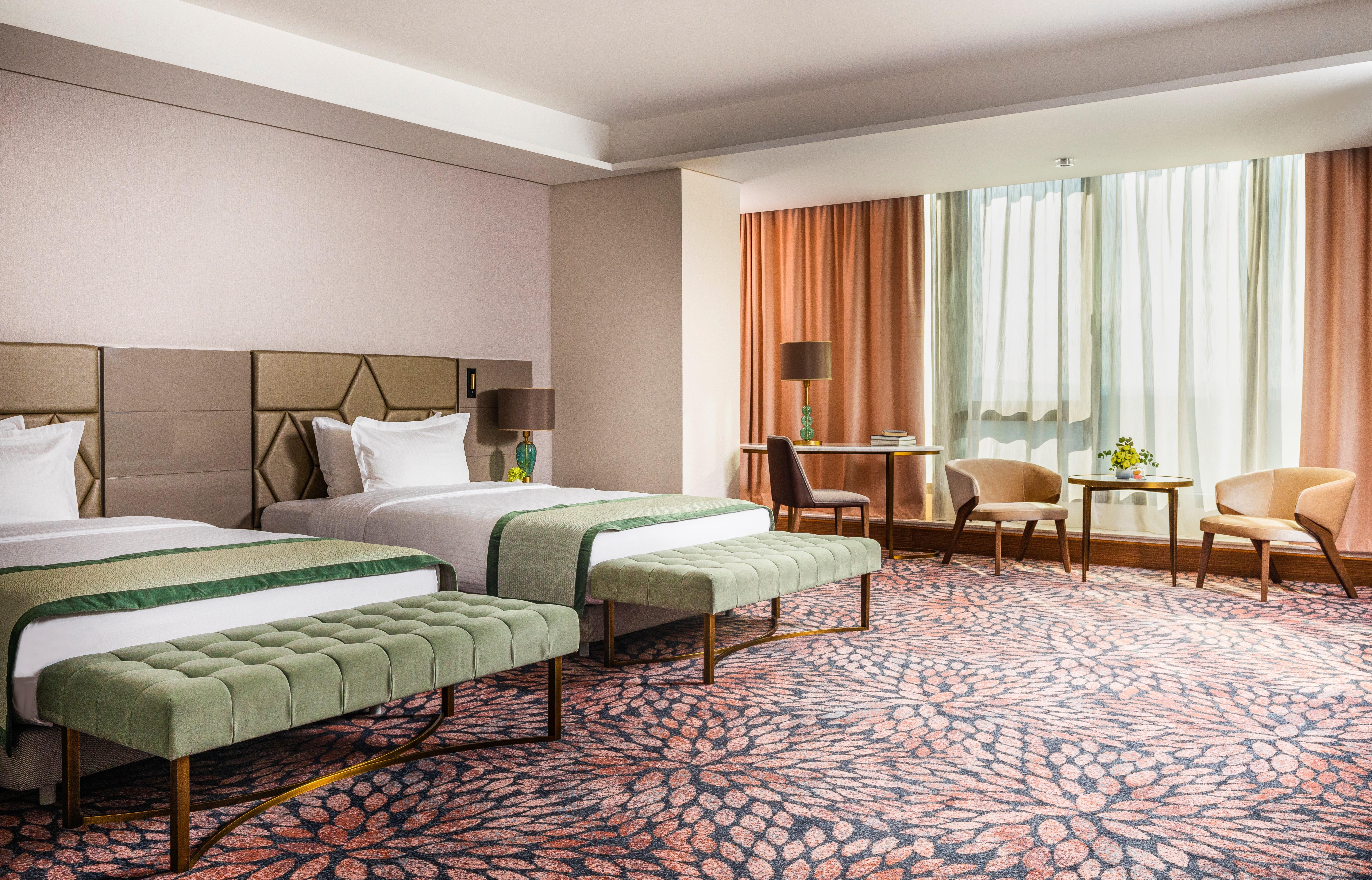 Grand Hotel Millennium Sofia Bagian luar foto The image shows a well-decorated hotel room featuring two beds with green striped bedspreads. There is a plush green bench at the foot of each bed. The room has large windows with sheer curtains allowing natural light to enter. There is a cozy seatin