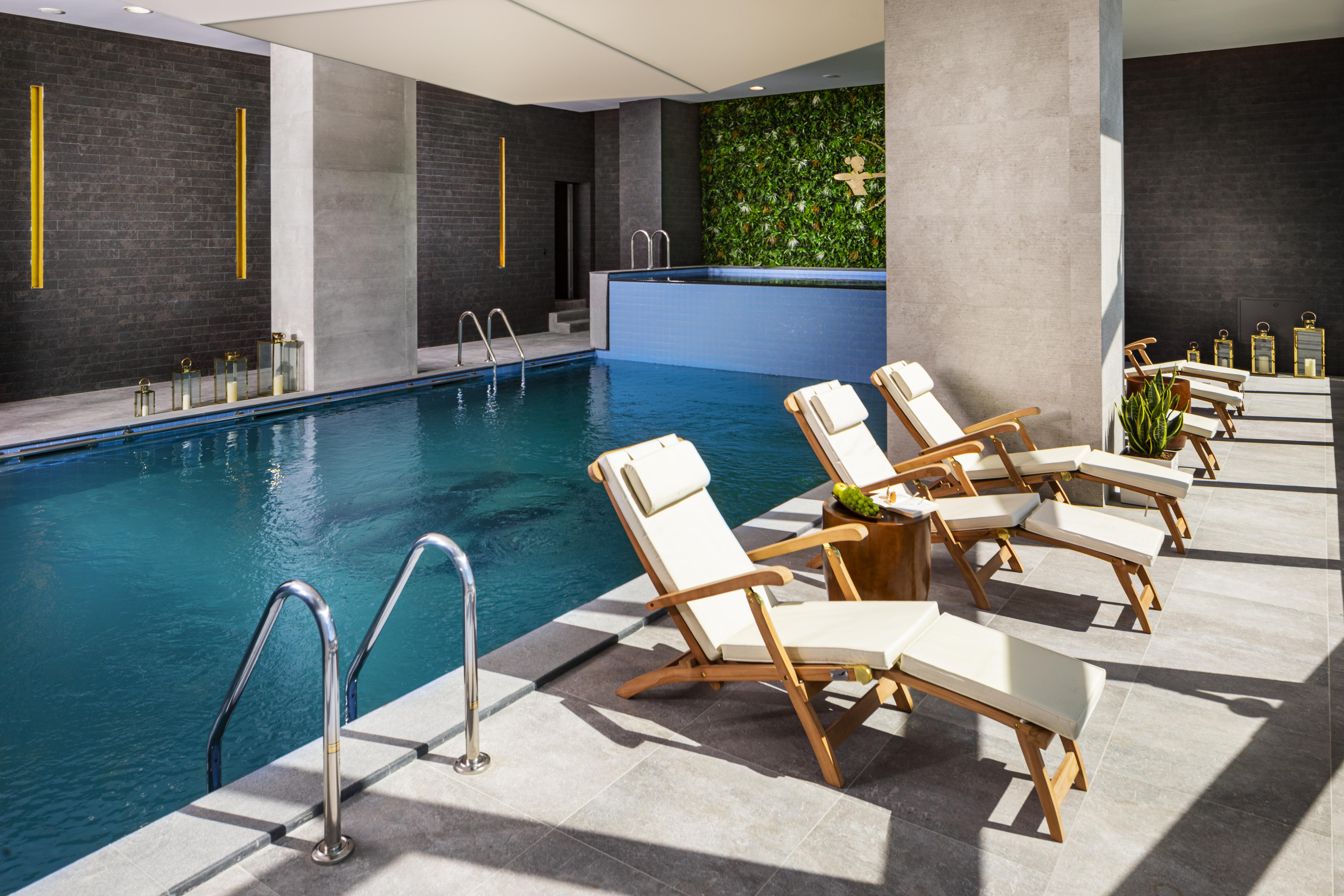 Grand Hotel Millennium Sofia Bagian luar foto The photo shows a serene indoor swimming pool area. The pool is clear and inviting, with a blue water surface reflecting light. Along one side of the pool, there are several light-colored lounge chairs with white cushions, positioned for relaxation. 