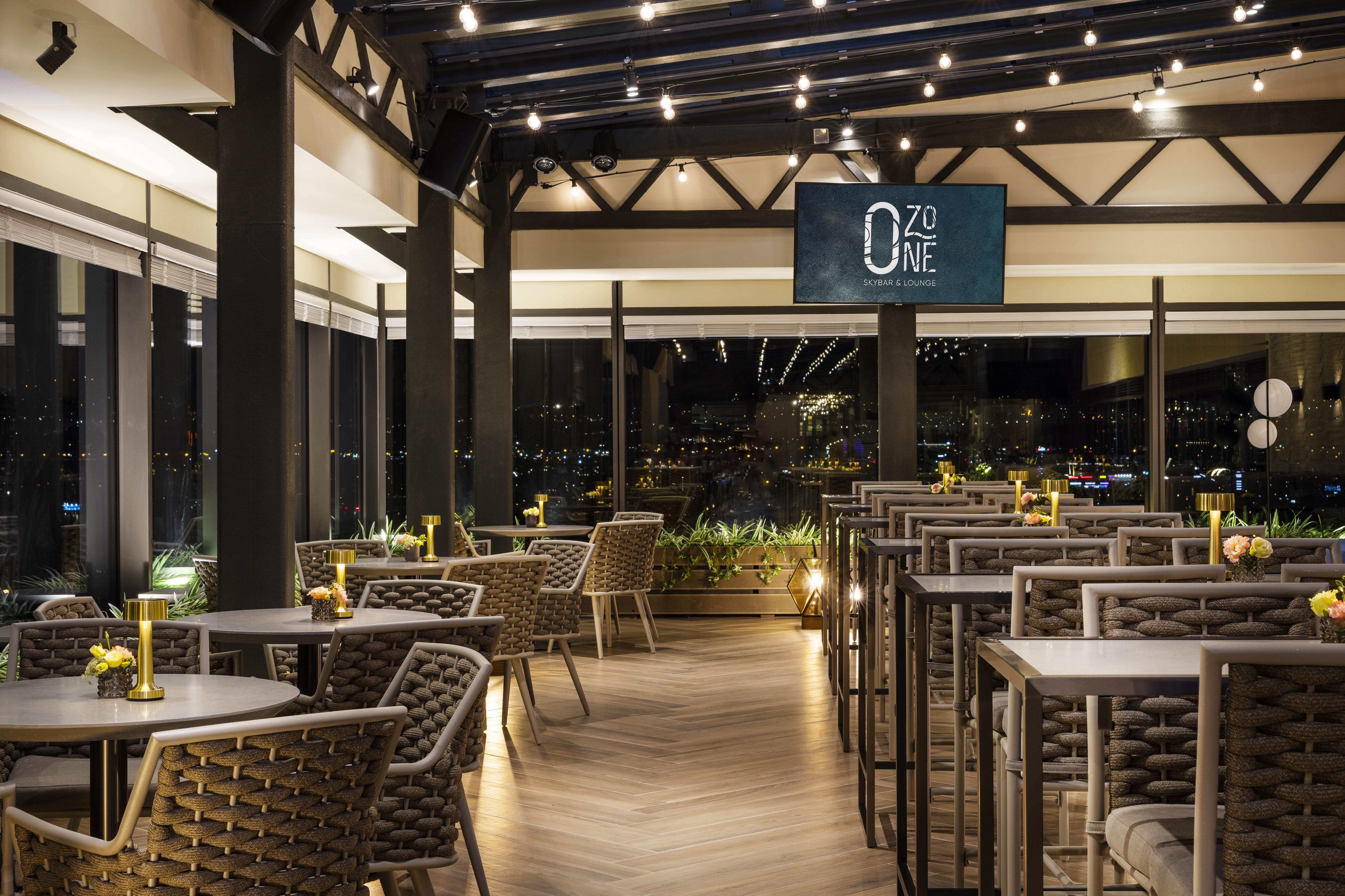Grand Hotel Millennium Sofia Bagian luar foto The photo depicts a modern restaurant interior with a stylish design. The space features a series of tables and chairs arranged neatly, with a clean and sophisticated aesthetic. The tables are set with small yellow flowers, adding a touch of color to